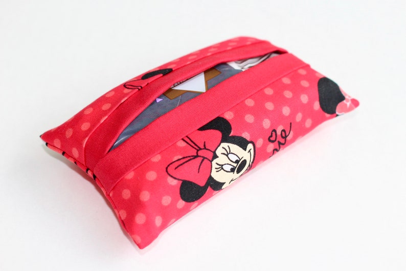 May include: A rectangular tissue holder featuring a red fabric with white polka dots and a Minnie Mouse design. The holder has a red band across the top and a slot for tissue dispensing.