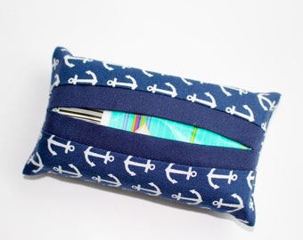 May include: A navy blue tissue box cover with a white anchor pattern. The cover has a rectangular shape with a dark blue band across the top and bottom. The tissue opening is visible in the centre.