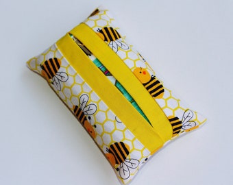 May include: A rectangular tissue box cover featuring a yellow and white honeycomb pattern with cartoon bees. Two yellow bands are across the top. The cover is designed to hold a standard tissue box, adding a decorative touch to any room.