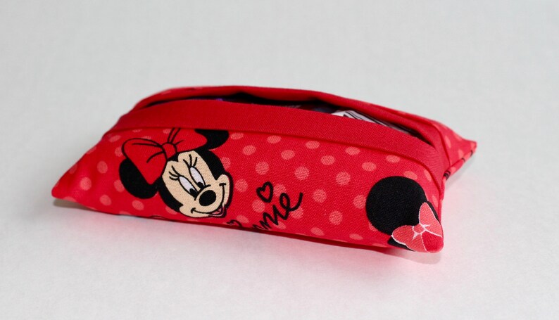 May include: Red fabric pouch with a Minnie Mouse design. The pouch features a red polka dot pattern and a Minnie Mouse graphic on the front. The pouch has a red zipper and is rectangular in shape.