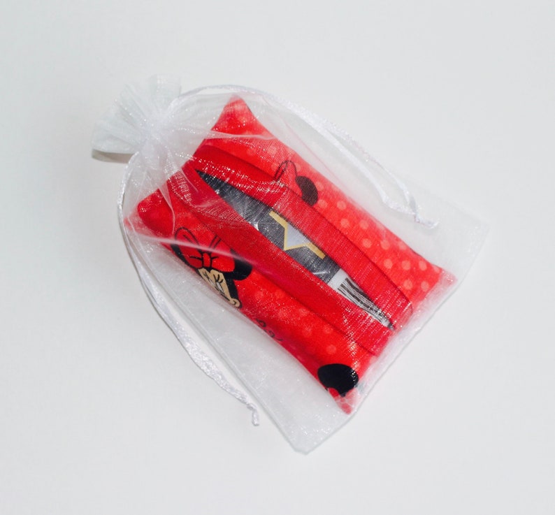 May include: A small, white, sheer drawstring bag containing several red fabric items. The red fabric has a polka dot pattern and a Minnie Mouse graphic. The bag is tied with a white ribbon.