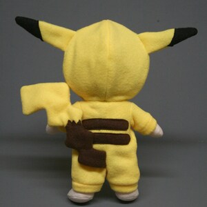 May include: Yellow plush toy in the shape of a Pikachu, a popular Pokemon character. The toy is wearing a brown and yellow jumpsuit with a brown tail.