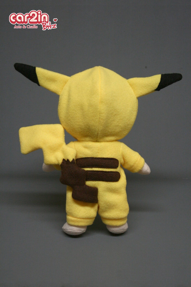 May include: Yellow plush toy in the shape of a Pikachu, a popular Pokemon character. The toy is wearing a brown and yellow jumpsuit with a brown tail.