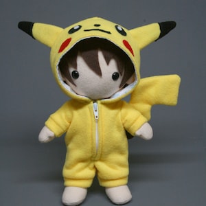 May include: A yellow plush toy wearing a Pikachu costume. The toy has brown hair, a white face, and black eyes. The costume has red cheeks and a black tail.