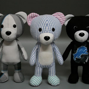 May include: Three handmade teddy bears. One is gray and white plaid, the second is blue and white striped, and the third is black with a blue and silver logo. Each bear has a black nose and button eyes.