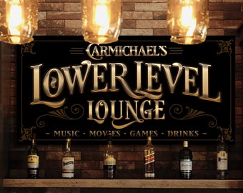 May include: A black sign with gold lettering that reads "Carmichael's Lower Level Lounge - Music - Movies - Games - Drinks -" hanging above a bar with bottles of liquor on a shelf.
