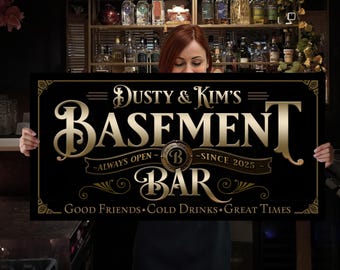 May include: A black rectangular sign with gold lettering that reads "Dusty & Kim's Basement Bar". The sign includes the text "Always Open - Since 2025" and "Good Friends, Cold Drinks, Great Times". The sign is held by a person.