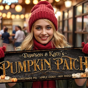 May include: A woman holds a sign for "Dawson & Kate's Pumpkin Patch." The sign is black with gold lettering and features pumpkins. She wears a red hat, scarf, and gloves. The background is blurred, suggesting an outdoor market setting.