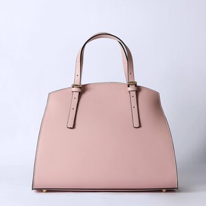 Pu&ograve; includere: Una borsa tote in pelle rosa chiaro con cinturini neri e dettagli dorati.