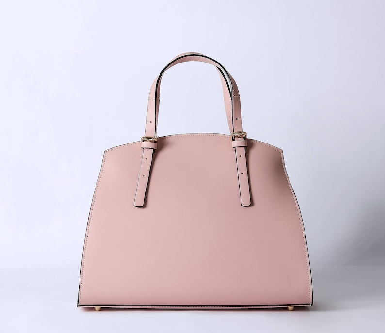 Pu&ograve; includere: Una borsa tote in pelle rosa chiaro con cinturini neri e dettagli dorati.