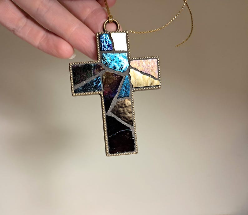 Peut inclure: Une d&eacute;coration de No&euml;l en forme de croix en verre color&eacute; avec une bordure dor&eacute;e et un motif bleu, violet et or. La croix est suspendue &agrave; une ficelle dor&eacute;e.