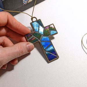Peut inclure: Un pendentif en forme de croix en verre mosa&iuml;que bleu et vert avec un cadre en m&eacute;tal dor&eacute;. La croix est suspendue &agrave; un cordon dor&eacute;.