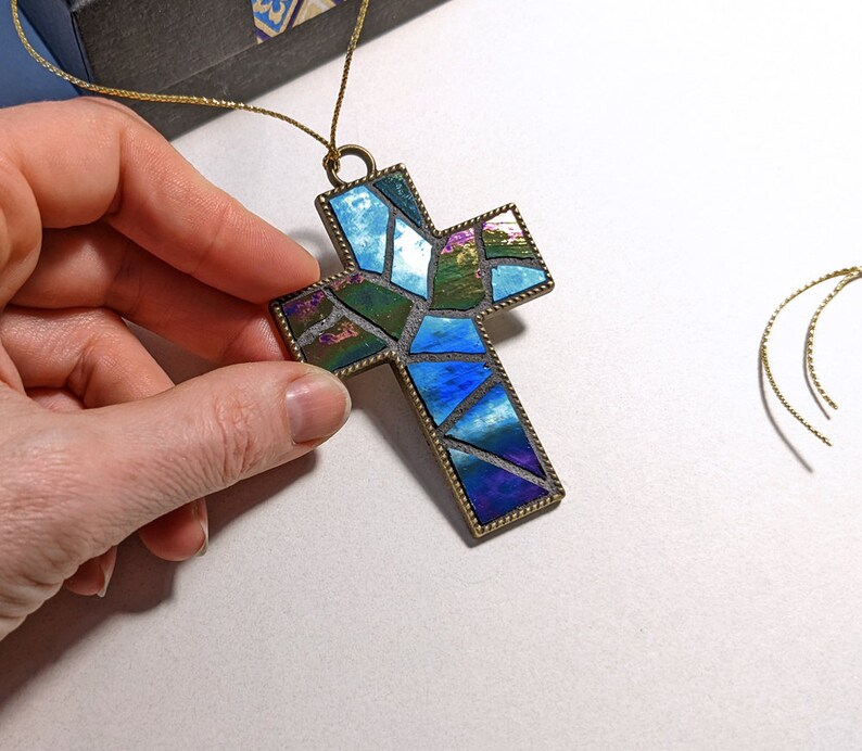 Peut inclure: Un pendentif en forme de croix en verre mosa&iuml;que bleu et vert avec un cadre en m&eacute;tal dor&eacute;. La croix est suspendue &agrave; un cordon dor&eacute;.