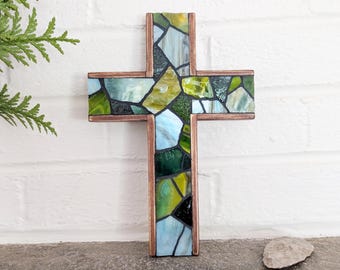 Peut inclure: Une croix murale composée d'un cadre en métal cuivré rempli d'une mosaïque de morceaux de verre teinté dans des tons de vert, bleu clair et jaune, séparés par des lignes de joint sombres sur toute la surface de l'objet.