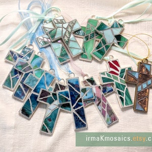 Peut inclure: Assortiment d'ornements en forme de croix en mosa&iuml;que de verre de diff&eacute;rentes couleurs, notamment bleu, vert, rouge et marron. Chaque croix est encadr&eacute;e d'argent et poss&egrave;de une petite boucle pour la suspendre. Les ornements sont pr&eacute;sent&eacute;s sur un fond en tissu blanc avec des rubans.