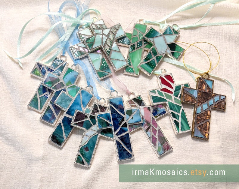 Peut inclure: Assortiment d'ornements en forme de croix en mosa&iuml;que de verre de diff&eacute;rentes couleurs, notamment bleu, vert, rouge et marron. Chaque croix est encadr&eacute;e d'argent et poss&egrave;de une petite boucle pour la suspendre. Les ornements sont pr&eacute;sent&eacute;s sur un fond en tissu blanc avec des rubans.