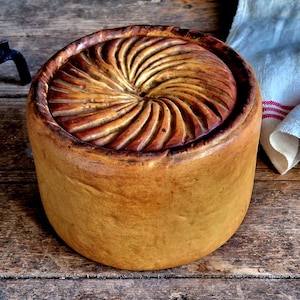 May include: A large, round, golden brown pie crust with a decorative swirl pattern on top. The crust is sitting on a wooden surface.