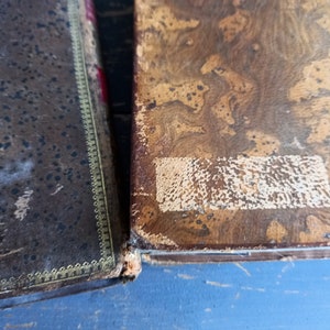 Op de afbeelding: Twee antieke boeken met bruine lederen omslagen. Het boek links heeft een gouden rand en het boek rechts heeft een bruin en wit marmermotief.