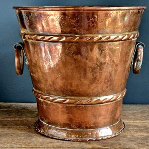May include: A vintage copper ice bucket with two handles. The bucket has a hammered finish and a decorative band around the top.