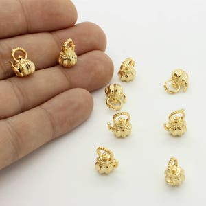 May include: A collection of ten gold-colored teapot charms. The charms are small and detailed, with a classic teapot shape.
