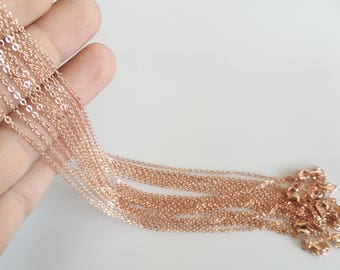 May include: A bundle of rose gold chain necklaces with lobster clasps. The chains are arranged in a fan shape and are held in a hand.