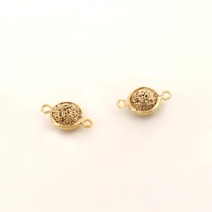 May include: Two gold-toned metal clasps with a decorative, intricate, woven design. Each clasp has two loops for attaching to a necklace or bracelet.