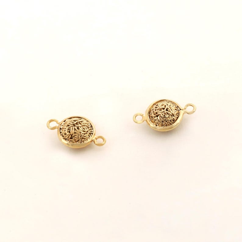 May include: Two gold-toned metal clasps with a decorative, intricate, woven design. Each clasp has two loops for attaching to a necklace or bracelet.