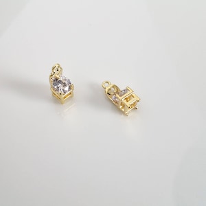 Puede incluir: Dos colgantes de tono dorado con piedras de circonita cúbica transparentes. Los colgantes están diseñados para ser unidos a un collar o pulsera.