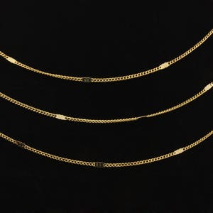 May include: Four gold chains with oval-shaped links layered on a black background.