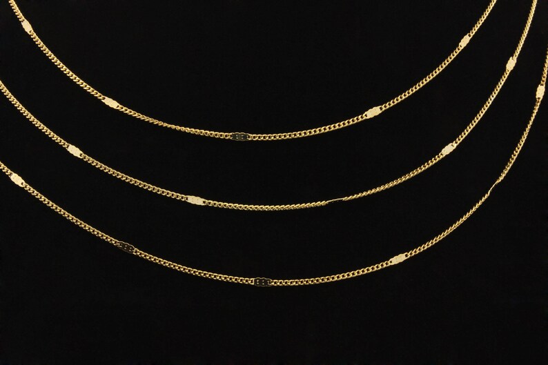 May include: Four gold chains with oval-shaped links layered on a black background.