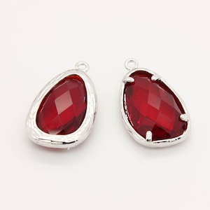 以下が含まれることがあります： 赤いファセットカットガラスの石が付いた銀色のペンダントチャーム2個。石は、テardropの形に、テクスチャ加工された銀の縁取りでセットされています。