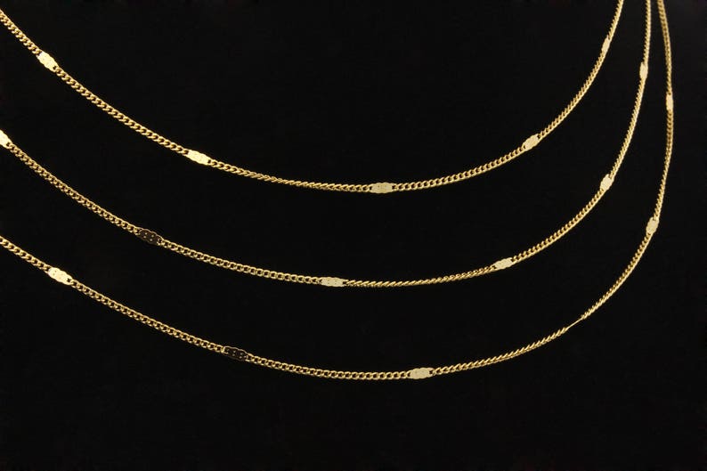 May include: Four gold chains with oval-shaped links, layered on a black background.