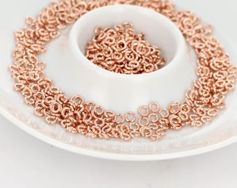 May include: Rose gold jump rings scattered on a white, two-tiered serving dish. The jump rings are small, circular, and metallic, with a bright, reflective finish. The dish has a simple, elegant design, with a shallow, round bowl in the center.
