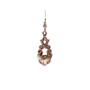 May include: A single, ornate, gold-colored earring. The earring features a decorative design with a shell-like bottom and a geometric top, connected by a delicate chain. The earring is designed to hang from a pierced ear.