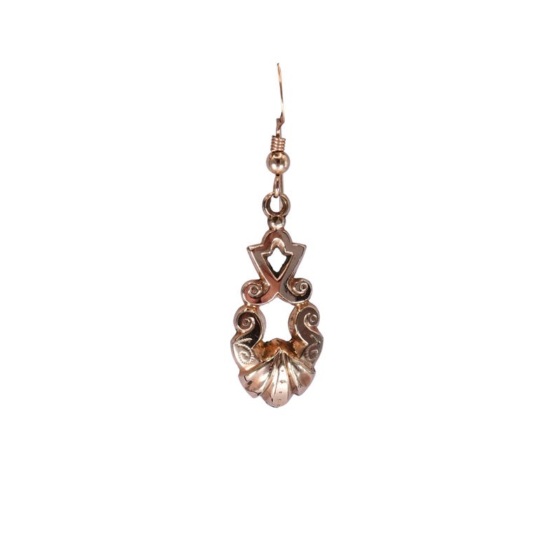 May include: A single, ornate, gold-colored earring. The earring features a decorative design with a shell-like bottom and a geometric top, connected by a delicate chain. The earring is designed to hang from a pierced ear.