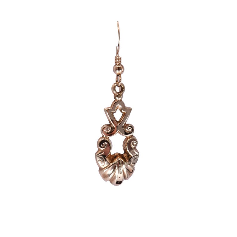 May include: A single, ornate gold earring with a decorative design. The earring features a hook, a series of small beads, and a detailed pendant with swirling patterns and a shell-like base. The earring is set against a white background.