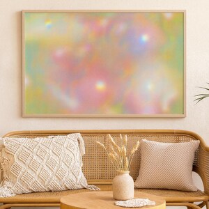 Puede incluir: Una impresión artística abstracta enmarcada con un diseño suave y borroso en colores pastel de rosa, amarillo y verde. La obra de arte cuelga sobre un sofá de mimbre con cojines decorativos y una mesa de madera.