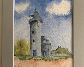 Puede incluir: Pintura acuarela de una torre de piedra gris con una puerta azul y un edificio gris más pequeño a su lado. Los edificios se encuentran sobre un fondo de cielo azul con nubes blancas y hierba verde.