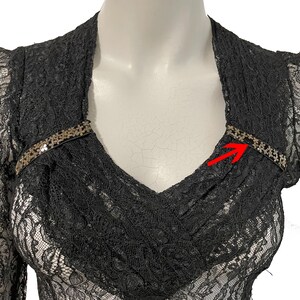 K&ouml;nnte beinhalten: Schwarzes Spitzentop mit langen &Auml;rmeln und V-Ausschnitt. Das Oberteil hat ein zartes Blumenmuster und ist mit einem dekorativen Paillettenband am Ausschnitt verziert. Das Kleidungsst&uuml;ck wird auf einer Schaufensterpuppe pr&auml;sentiert.