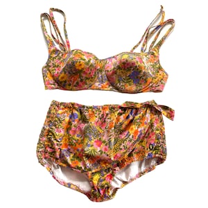 Może przedstawiać: Bikini w kwiatowy wzór z gorsetem i wysokimi majtkami. Gorset ma usztywniany biustonosz i regulowane ramiączka. Majtki mają wiązanie z boku.