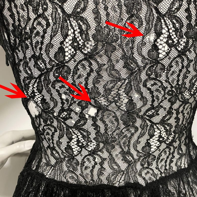 K&ouml;nnte beinhalten: Nahaufnahme eines schwarzen Spitzenkleides. Das komplizierte florale Spitzenmuster ist vor einem wei&szlig;en Hintergrund sichtbar. Das Kleid hat ein figurbetontes Oberteil und einen ausgestellten Rock mit zarter, strukturierter Optik.