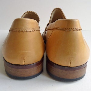 Puede incluir: Un par de mocasines de cuero color canela, vistos desde atr&aacute;s. Los zapatos tienen un tal&oacute;n redondeado, una parte superior cosida y una suela marr&oacute;n oscuro. El cuero tiene una textura suave.
