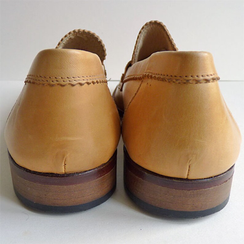 Puede incluir: Un par de mocasines de cuero color canela, vistos desde atr&aacute;s. Los zapatos tienen un tal&oacute;n redondeado, una parte superior cosida y una suela marr&oacute;n oscuro. El cuero tiene una textura suave.