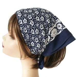 May include: A navy blue headscarf featuring a white paisley design and a white floral border. The headscarf is tied at the back. The edges of the fabric are folded over.