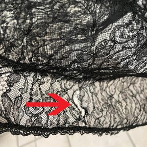 K&ouml;nnte beinhalten: Nahaufnahme eines schwarzen Spitzenstoffs. Die Spitze hat ein zartes Blumenmuster und einen gewellten Rand. Der Stoff ist leicht durchscheinend und gibt einen Blick auf den Hintergrund frei. Die Gesamtstruktur ist komplex und detailliert.