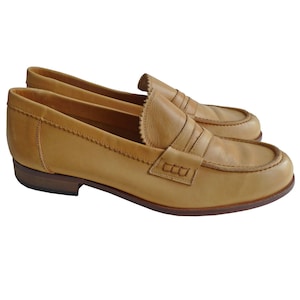 Puede incluir: Un par de mocasines penny de cuero color canela. Los zapatos tienen un dise&ntilde;o cl&aacute;sico con punta redonda, una correa en el empeine y un tac&oacute;n bajo. El cuero tiene una textura suave y un color c&aacute;lido y neutro.