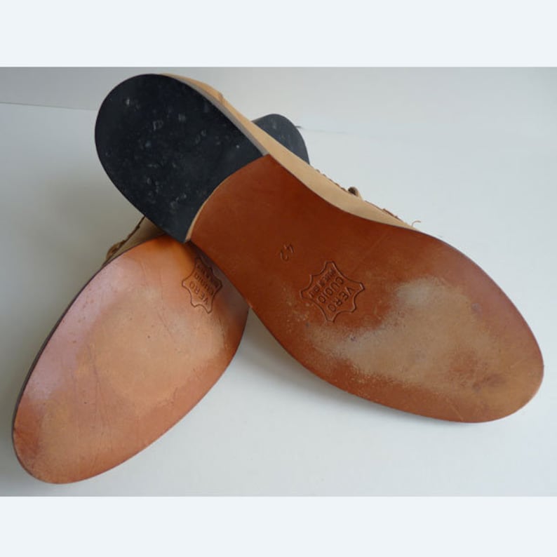 Puede incluir: Un par de zapatos de cuero color canela, con las suelas hacia arriba, con un tac&oacute;n negro y una suela de cuero marr&oacute;n. Las suelas est&aacute;n marcadas con "VERO CUOIO" y el n&uacute;mero "42". Los zapatos parecen nuevos.