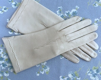 Könnte beinhalten: Ein Paar cremefarbene Lederhandschuhe mit einem gewellten Rand und dekorativen Nähten.