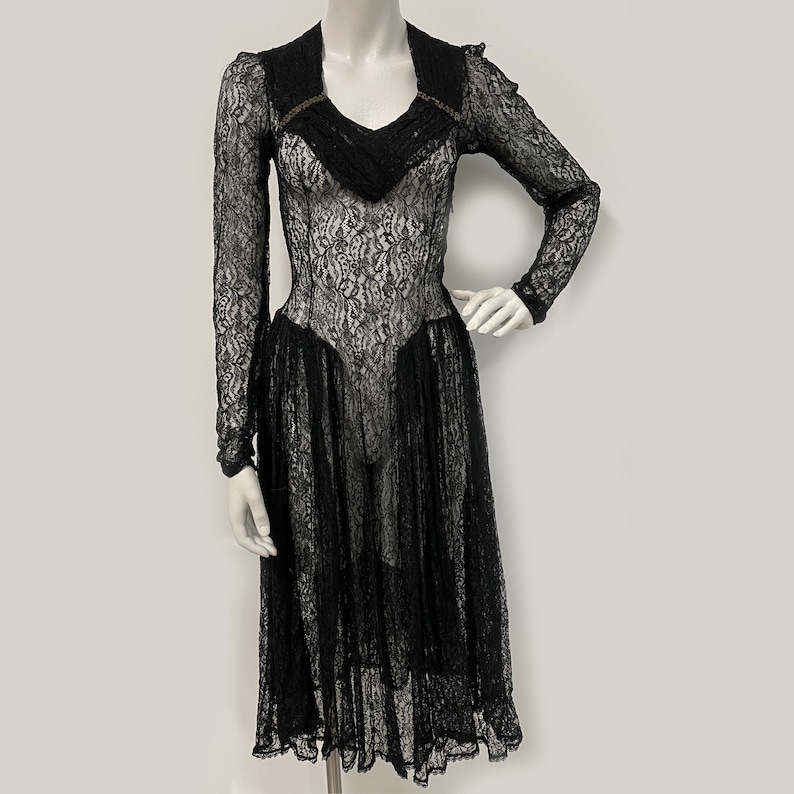 K&ouml;nnte beinhalten: Schwarzes Spitzenkleid mit langen &Auml;rmeln und V-Ausschnitt. Das Kleid hat ein figurbetontes Oberteil und einen ausgestellten Rock, der eine elegante Silhouette schafft. Die aufwendigen Spitzendetails verleihen dieser Abendgarderobe einen Hauch von Vintage-Charme.