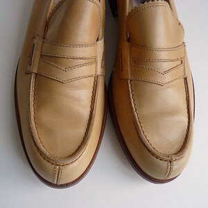 Puede incluir: Un par de mocasines penny de cuero color beige claro. Los zapatos tienen un dise&ntilde;o cl&aacute;sico con una correa en el empeine y una suela cosida. El cuero tiene una textura suave y un ligero brillo.